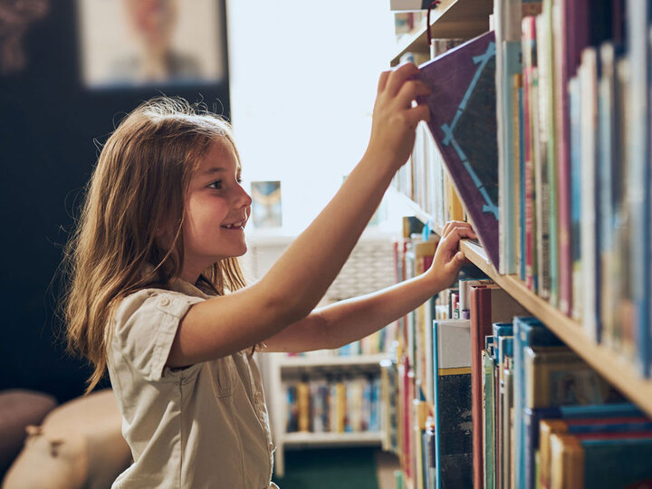 Girl getting a book from a bookshelf.